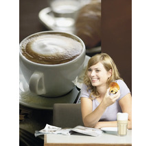 Een vrouw zit aan een tafel met koffie, een chocoladecroissant en een tijdschrift.