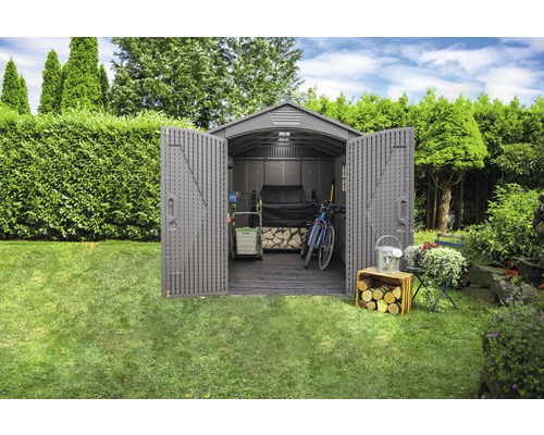 Tuin met open gereedschapsschuur met tuingereedschap, een fiets en houtopslag.