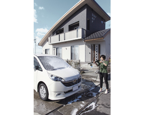 Vrouw reinigt een auto met een hogedrukreiniger voor een huis.