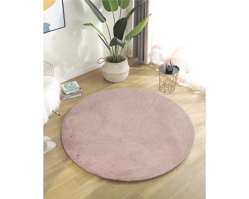 Rond, roze tapijt in een lichte woonkamer met potplant en bijzettafel