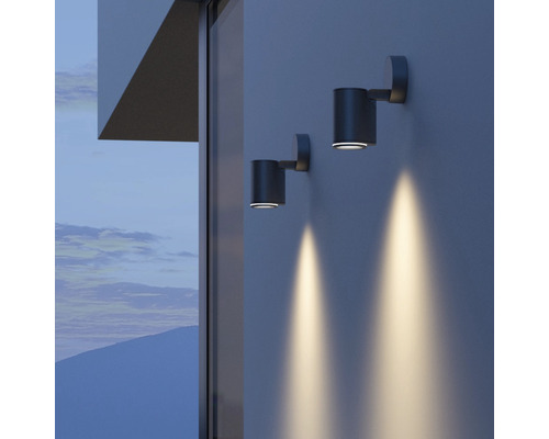 Twee grijze wandlampen verlichten een muur.