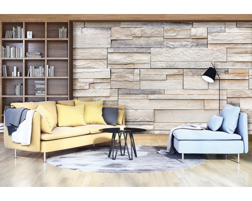 Woonkamer met boekenkast, bank, fauteuil, tafel, staande lamp en stenen muur