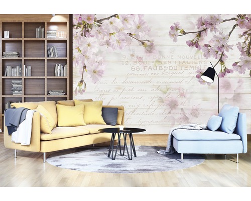 Woonkamer met bank, fauteuil, tafel en boekenkast voor een muurbehang met bloemmotieven