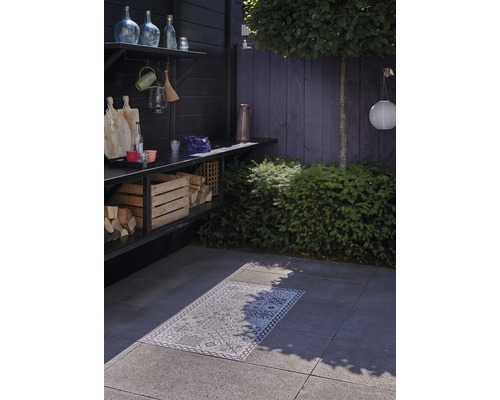 Buitenruimte met houtskoolbarbecue, houtopslag en decoratief tapijt op stenen tegels