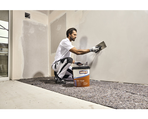 Ambachtsman brengt Modulan Fill plus Finish vulmiddel aan op een muur