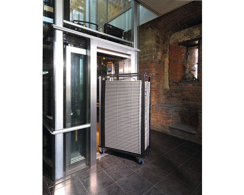 Een lift met een wagen vol platen in een gebouw.