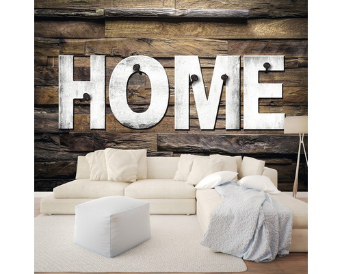 Woonkamer met bank, kruk en wanddecoratie met het woord HOME op houten panelen.