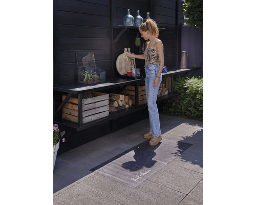 Scene met een buitenruimte met houten planken, decoraties en een vrouw die een snijplank vasthoudt.