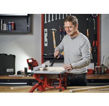 Man werkt met een tafelzaag in een werkplaats met gereedschap aan de muur.