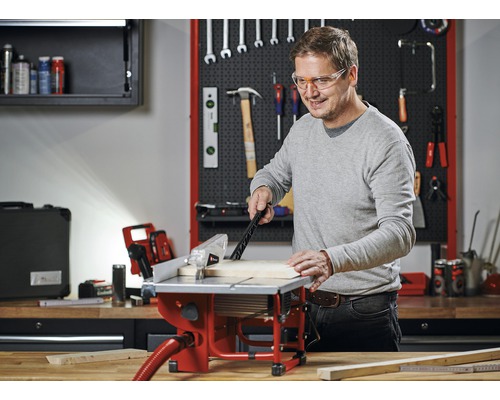Man werkt met een tafelzaag in een werkplaats met gereedschap aan de muur.