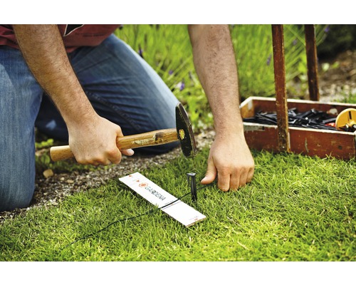 Persoon hamert haring met hamer in de grond om een Gardena Micro-Drip-System te bevestigen.