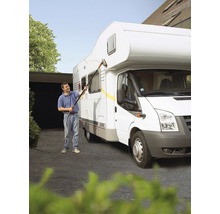 Een persoon reinigt een camper met een wasborstel en een slang.