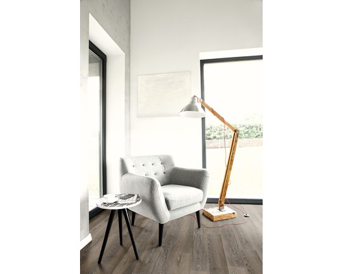 Lichte kamer met fauteuil, vloerlamp en kleine bijzettafel op laminaatvloer.
