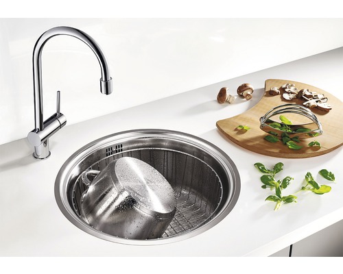 Keukenscène met ronde gootsteen, kraan, snijplank, pan en ingrediënten.