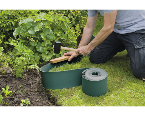 Persoon installeert groene gazonrand met hamer in de tuin.