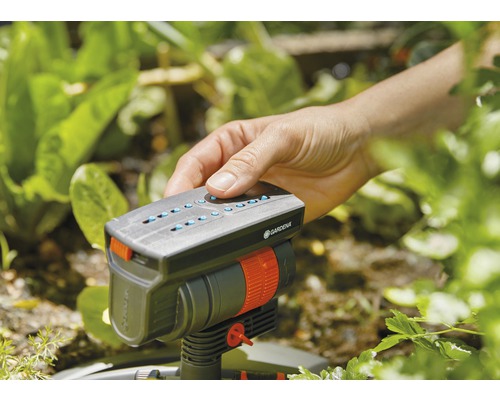 Een hand bedient een Gardena sproeier in de tuin.