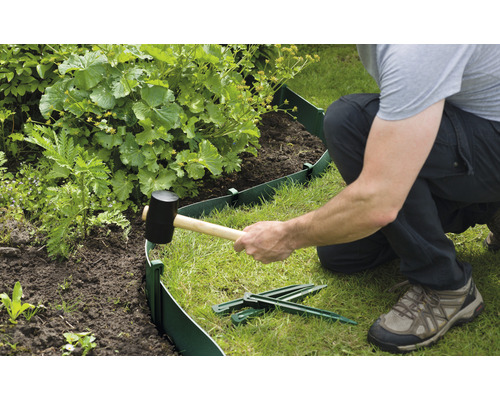 Een persoon installeert een groene gazonrand met een rubberen hamer in de tuin.