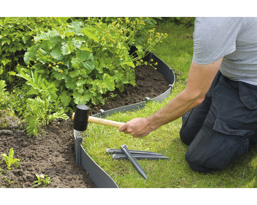 Installatie van een gazonrand met een rubberen hamer en grondankers in de tuin