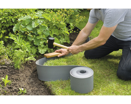 Iemand legt een gazonrand aan met een rubberen hamer in de tuin.
