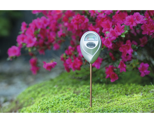 Bodemvochtmeter in een tuinperk met bloeiende planten op de achtergrond