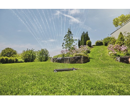 Gazonsproeier besproeit een groene tuin met bomen en planten