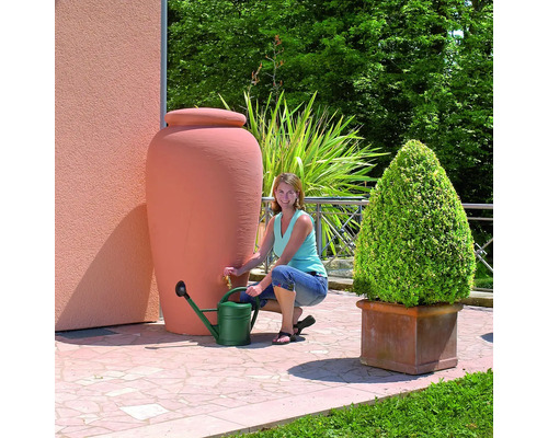 Vrouw vult een groene gieter bij een terracotta kleurige regenwatertank in de tuin.