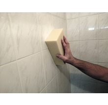 Een hand houdt een spons tegen een betegelde muur.