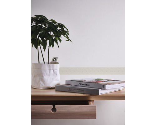 Scene met kamerplant in papieren zak, boeken, wandborduur en houten bureau met lade