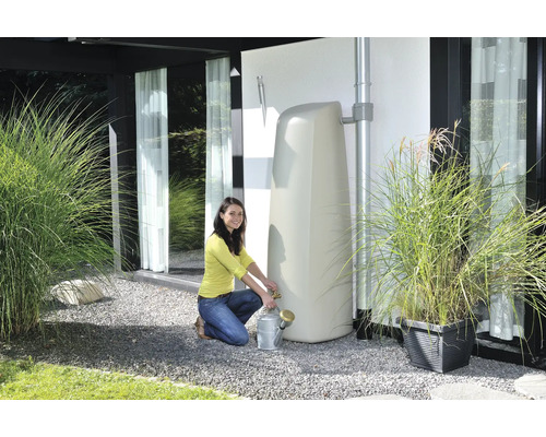 Vrouw vult een gieter bij een staande watertank in de tuin.