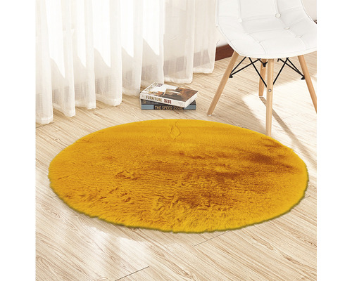Rond, geel imitatievacht tapijt op houten vloer naast een stoel