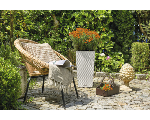 Tuinscene met rotan stoel, plantenbak en decoratie op stenen vloer