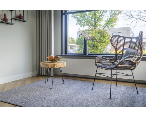 Woonkamer met rotan stoel, houten bijzettafel en grijs tapijt.