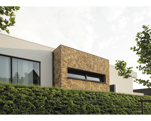 Buitenaanzicht van een modern huis met natuurstenen gevel en een begroeide helling