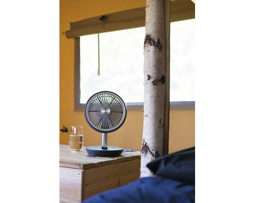 Tafelventilator op een houten tafel naast een glas water in een tent.