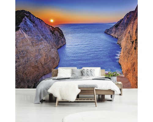 Wandafbeelding in slaapkamer met uitzicht op zee tussen kliffen bij zonsondergang.