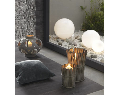 Decoratieve scène met lantaarn, kussen, windlichten van takken en tuinkogels op grind