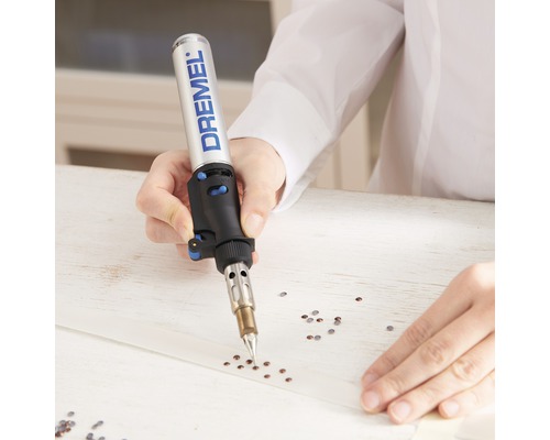 Een persoon gebruikt een Dremel-brander om strasssteentjes op een band aan te brengen.