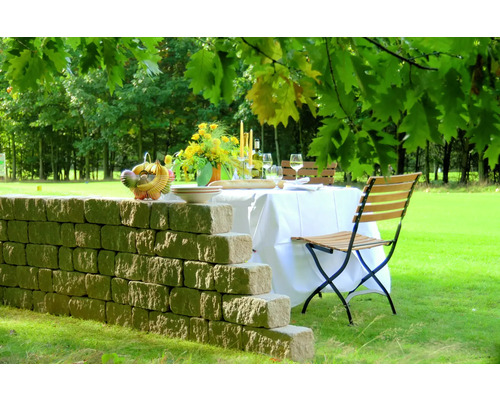 Gedekte tafel in de tuin met stenen muur, stoelen, bloemen en gerechten.