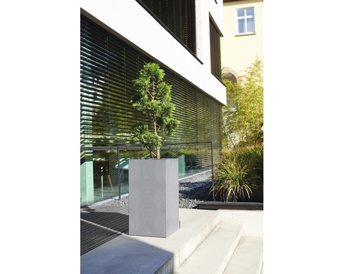 Grijze plantenbak met plant op een buitentrap voor een gebouw.