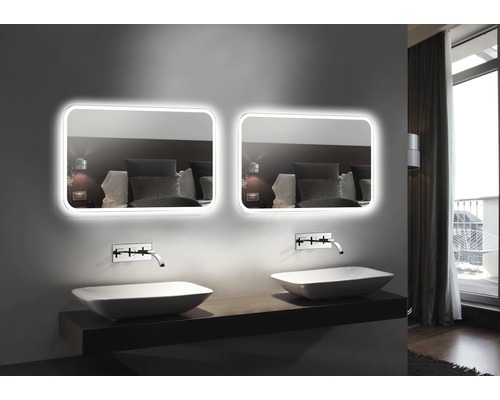 Badkamer met twee verlichte spiegels, twee opzetwastafels en kranen.