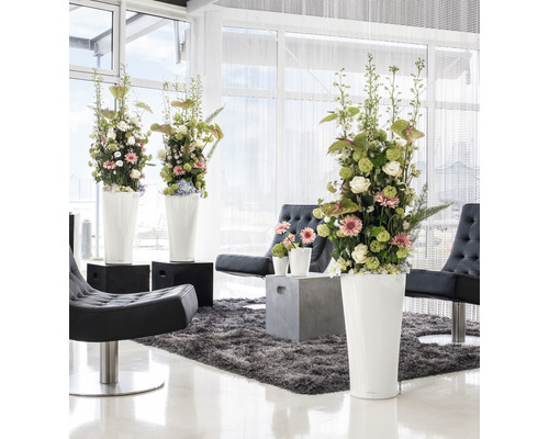 Licht interieur met bloemstukken in hoge plantenbakken, fauteuils en vloerkleed