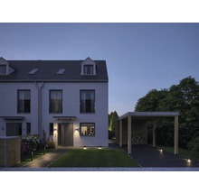 Aanzicht van een woonhuis met carport en tuinverlichting in de schemering.