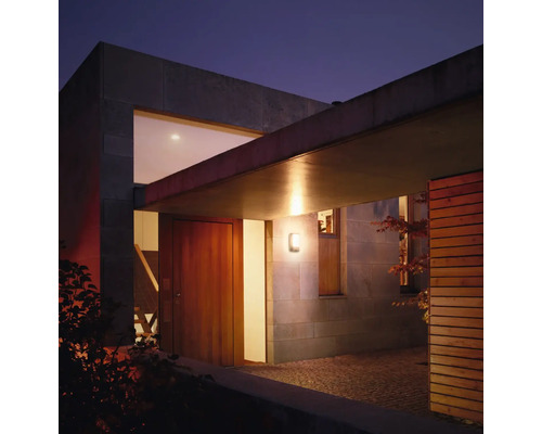 Verlichte woningentree met houten huis en stenen muur in de schemering.