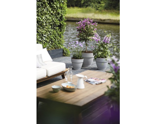 Terrasscène met houten tafel, zitplaatsen en beplante potten aan het water.