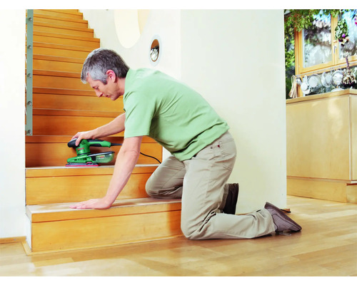 Man schuurt houten trap met een schuurmachine