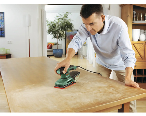 Man schuurt houten tafel met een vlakschuurmachine