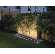 Verlichte tuinmuur met begroeiing en gazon.