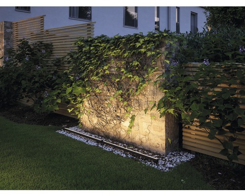 Verlichte tuinmuur met begroeiing en gazon.