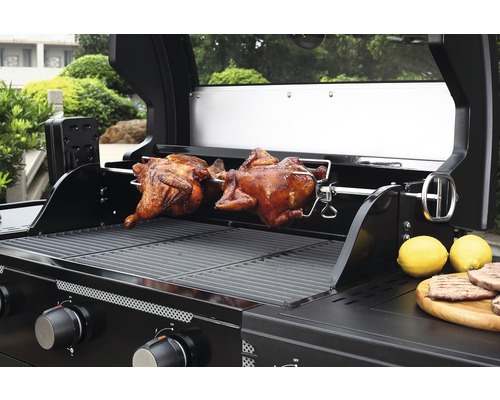 Gasbarbecue met twee gebraden kippen aan een draaispit en citroenen op een houten plank