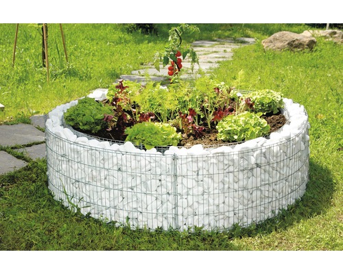 Ronde verhoogde tuinbak gemaakt van schanskorven gevuld met witte stenen in de tuin